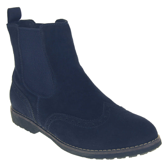 Navy suede brogue boots. Ankle boot style with brogue detailing. With a navy blue suede upper. Navy elasticated panels at the ankles and a blue loop at the heel to help pull them on. Black coloured sole with a very slight heel. Right foot at an angle.