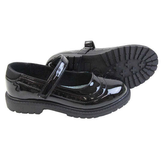 Older girls school shoes. Mary Jane style shoes with black patent faux leather uppers. With a touch fasten strap over the foot and brogue detailing around the top of the shoe. Black textile lining with a metallic blue insole. Chunky black sole with slight heel. Both feet from a side profile with the left foot on its side behind the the right foot to show the sole.