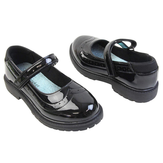 Older girls school shoes. Mary Jane style shoes with black patent faux leather uppers. With a touch fasten strap over the foot and brogue detailing around the top of the shoe. Black textile lining with a metallic blue insole. Chunky black sole with slight heel. Both feet at an angle facing top to tail.