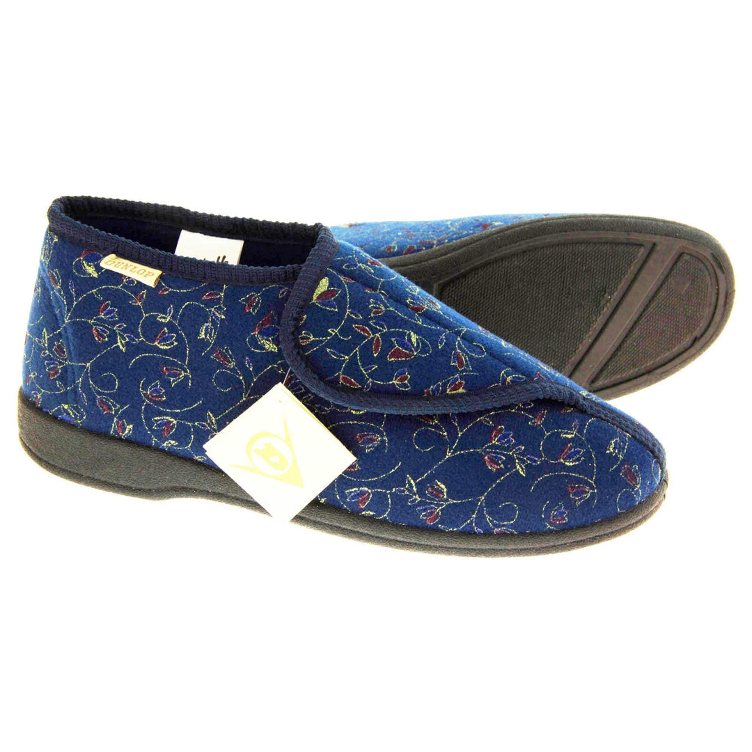 Orthopaedic slippers. Womens bootie style slipper with a navy blue textile upper with vine and flower embroidered design. Touch fasten tab to the top and blue textile lining. Firm black sole. Both feet from a side profile with the left foot on its side behind the the right foot to show the sole.