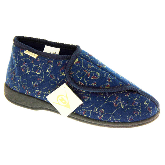 Orthopaedic slippers. Womens bootie style slipper with a navy blue textile upper with vine and flower embroidered design. Touch fasten tab to the top and blue textile lining. Firm black sole. Right foot at an angle.
