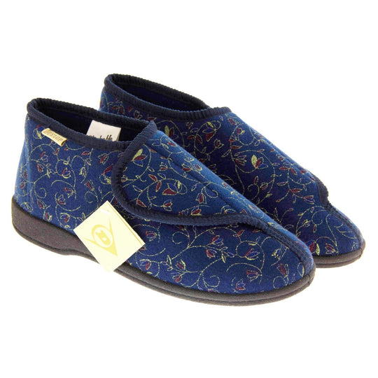 Orthopaedic slippers. Womens bootie style slipper with a navy blue textile upper with vine and flower embroidered design. Touch fasten tab to the top and blue textile lining. Firm black sole. Both feet together at angle.