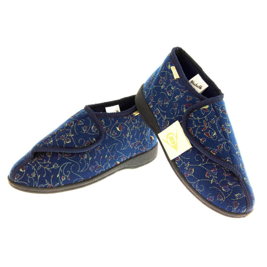 Orthopaedic slippers. Womens bootie style slipper with a navy blue textile upper with vine and flower embroidered design. Touch fasten tab to the top and blue textile lining. Firm black sole. Both feet in a v shape with the back of the right foot lifted on top of the left.