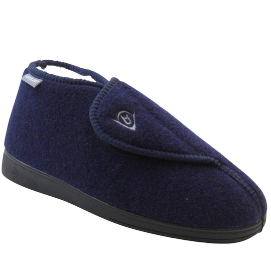 Orthopaedic slippers. Mens orthopaedic slippers in an ankle boot style. With a navy blue felt upper and white fleece lining. With an adjustable touch close top with a grey Dunlop logo on. Small grey label to the outer side edge with Dunlop written on. Thick black outdoor sole. Right foot at an angle.