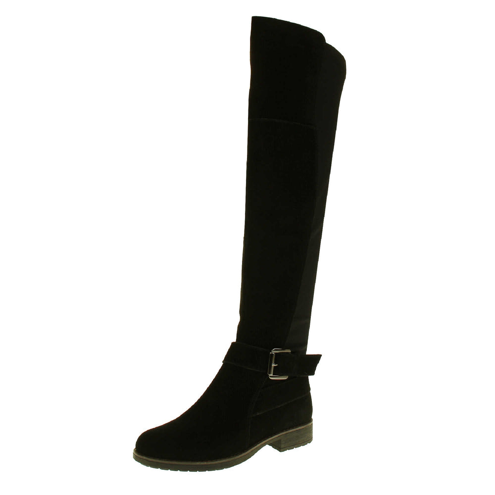 Over the knee flat suede boots. Tall boots that go above the knee in a black suede upper. Strap with buckle around the ankle. Black outsole with slight heel. Left foot at an angle.