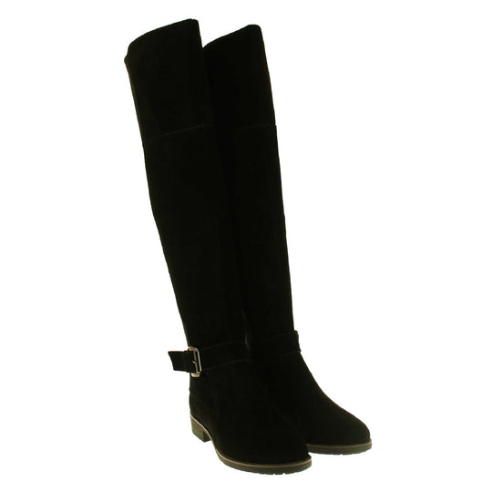 Over the knee flat suede boots. Tall boots that go above the knee in a black suede upper. Strap with buckle around the ankle. Black outsole with slight heel. Both feet together from an angle.