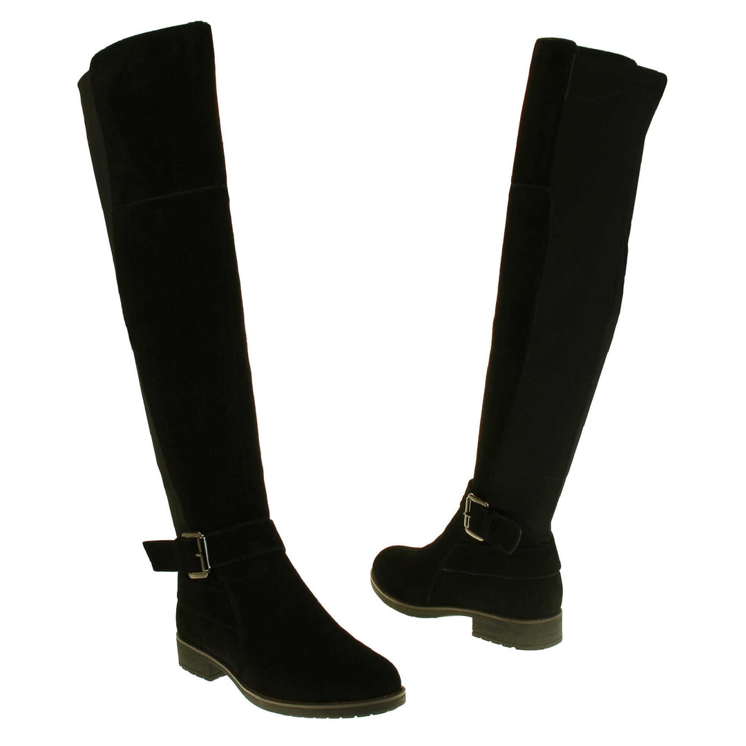Over the knee flat suede boots. Tall boots that go above the knee in a black suede upper. Strap with buckle around the ankle. Black outsole with slight heel. Both feet from a slight angle facing top to tail.