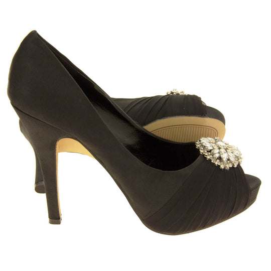 Peep toe black heels. Classic women's peep toe high heels with a black satin upper. Black insole with Sabatine branding. Black satin stiletto heel with a cream sole. Diamante cluster and ruched detailing across the toes. Both feet from a side profile with the left foot on its side behind the the right foot to show the sole.