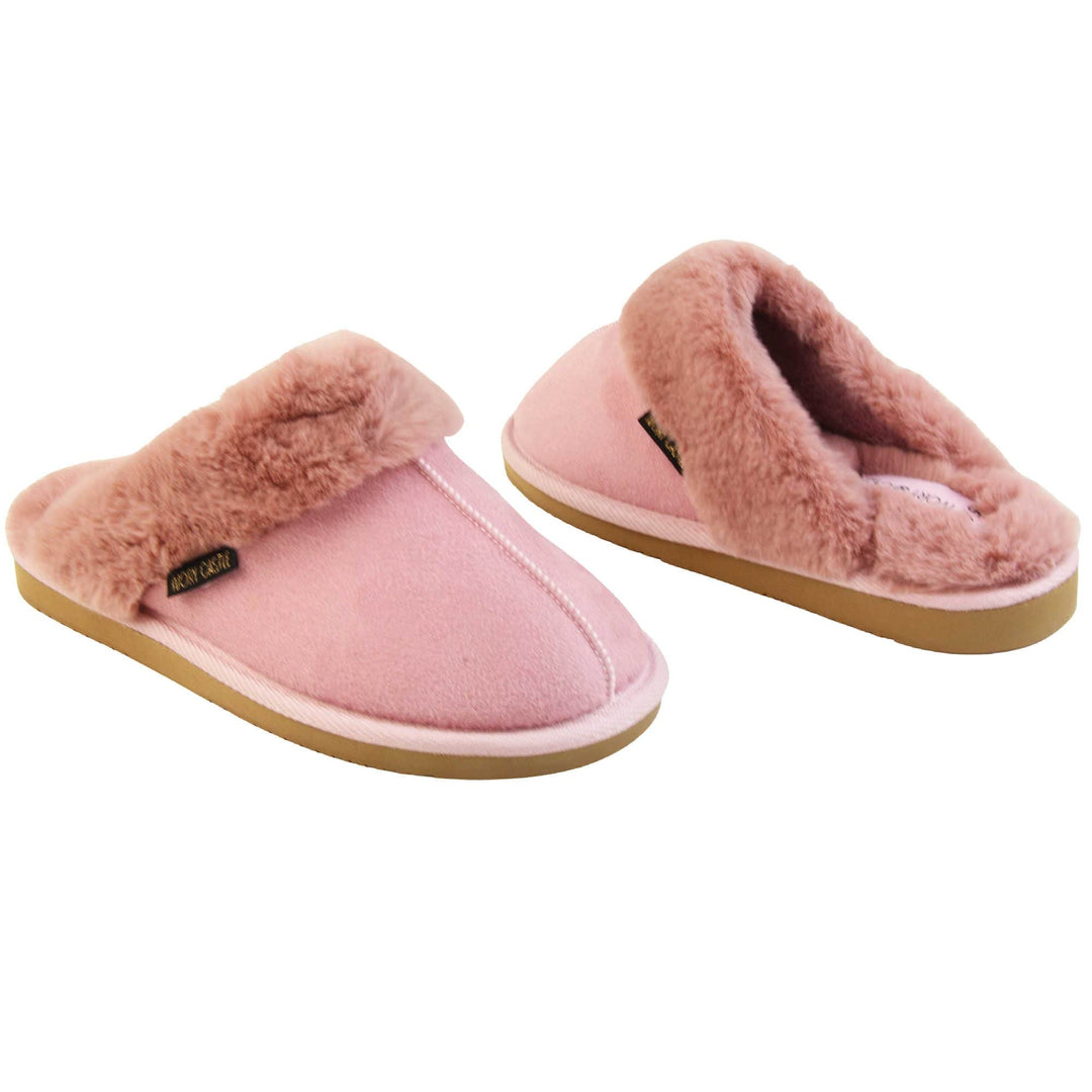 Pink Mule Slippers. Mule style slippers with pink faux suede uppers. Pink faux fur lining and collar. Firm pink outsole with grip on the bottom. Both feet at an angle, facing top to tail.