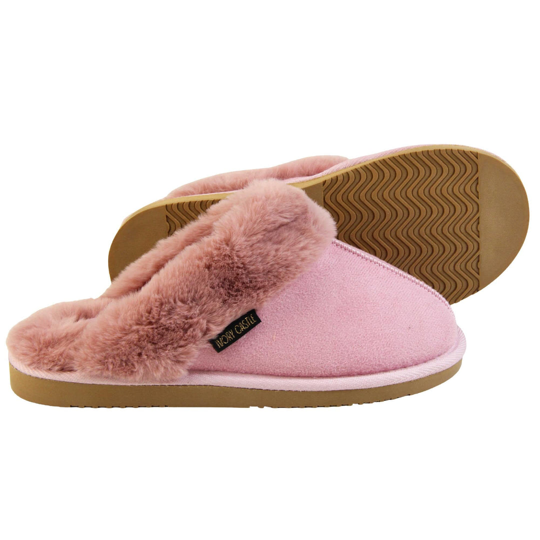 Pink Mule Slippers. Mule style slippers with pink faux suede uppers. Pink faux fur lining and collar. Firm pink outsole with grip on the bottom. Both feet from a side profile with the left foot on its side behind the the right foot to show the sole.