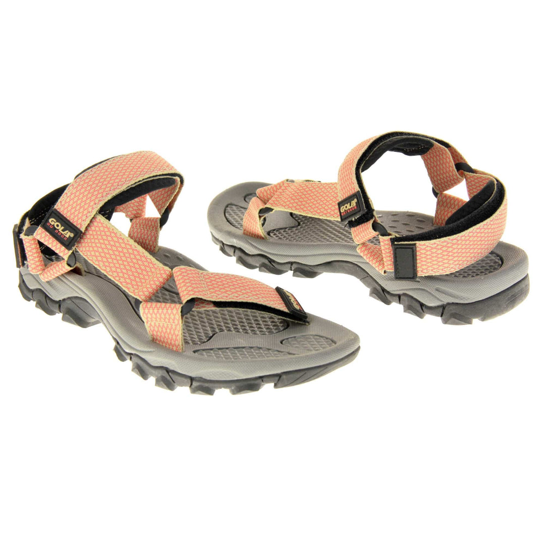 Pink walking sandals. Womens sporty style sandals. Beige textile straps with pink criss-cross pattern. Black padding to the heel and over foot strap. Touch fasten strap around the heel. Black Gola branding to the ankle of the sandal. Grey textile lining and black sole with chunky grip to the base. Both feet at an angle facing top to tail.