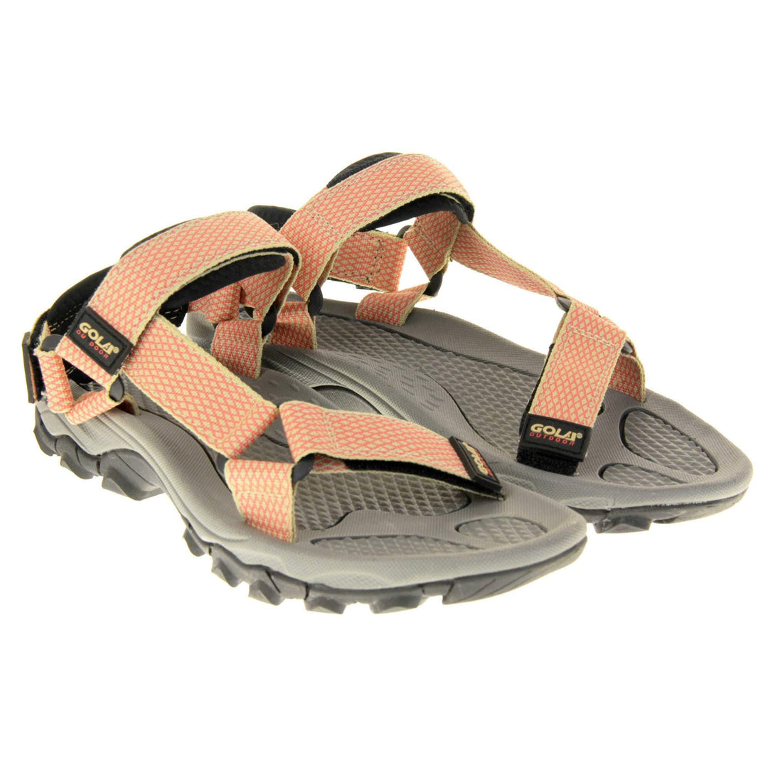 Pink walking sandals. Womens sporty style sandals. Beige textile straps with pink criss-cross pattern. Black padding to the heel and over foot strap. Touch fasten strap around the heel. Black Gola branding to the ankle of the sandal. Grey textile lining and black sole with chunky grip to the base. Both feet together at a slight angle.