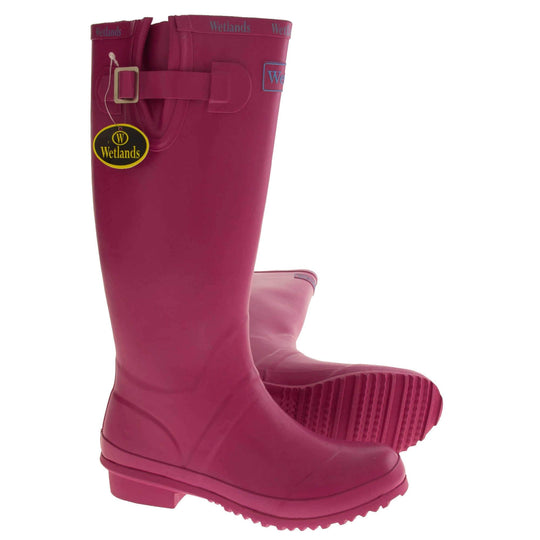 Pink wellington boots. Bright pink rubber waterproof wellington boots. Just below knee height. With a small heel and deep tread to the sole. Pink Wetlands Brand to the front of the boot near the top. Wetlands written in Lilac numerous times around the rim of the boot. Side strap with buckle to adjust the calf width. Textile lining to the inside of the boot. Both feet from a side profile but with the left foot on it side to show you the sole.