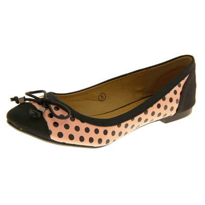 Polka dot flats. Womens ballerina style shoes with a glossy peach upper with black polka dots covering it. Black faux suede toes and heels and a black bow to the top. Nude faux-leather lining. Black sole with very slight heel. Left foot at an angle.