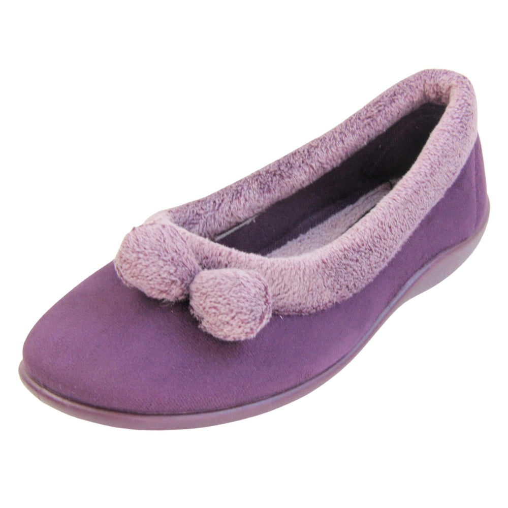 Pom pom slippers. Womens ballerina style slippers with purple velour uppers. Pale purple plush textile collar and two pom poms to the front of the shoe. Matching textile lining. Firm purple sole. Left foot at an angle.