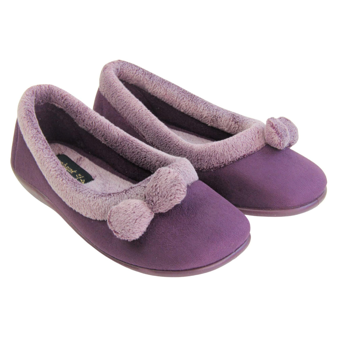 Pom pom slippers. Womens ballerina style slippers with purple velour uppers. Pale purple plush textile collar and two pom poms to the front of the shoe. Matching textile lining. Firm purple sole. Both feet together at an angle.