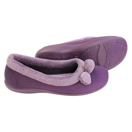 Pom pom slippers. Womens ballerina style slippers with purple velour uppers. Pale purple plush textile collar and two pom poms to the front of the shoe. Matching textile lining. Firm purple sole. Both feet from a side profile with the left foot on its side behind the the right foot to show the sole.