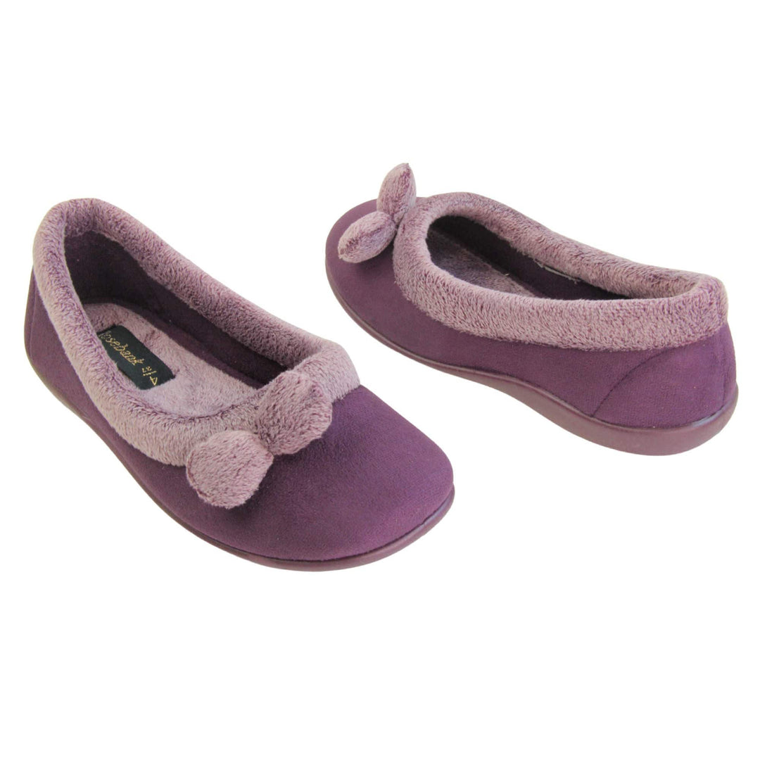 Pom pom slippers. Womens ballerina style slippers with purple velour uppers. Pale purple plush textile collar and two pom poms to the front of the shoe. Matching textile lining. Firm purple sole. Both feet at an angle facing top to tail.