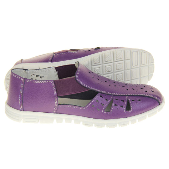 Purple wide fit shoes. Womens classic full foot sandal with a purple leather upper. Strappy sides with cut out designs along the side and centre straps. Purple elasticated straps joining the centre to the backs. White insole and leather lining. White sole with grip to the bottom. Both feet from a side profile with left foot on its side behind the right to show the sole.