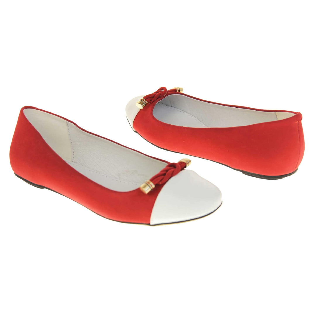 Red ballet flats. Womens ballerina style shoes with a red faux suede upper with white toe. Braided red rope detail to the top with gold studs to the end. White real leather lining and black sole.  Both feet at an angle facing top to tail.