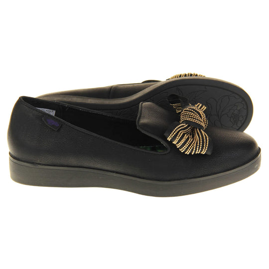 Rocket Dog slip on shoes. Loafer style shoes with a black faux leather upper. With a black and gold bow detail on the top of the foot. Bright floral patterned insole. Chunky black sole with slip resistant grip to the bottom. Both feet from a side profile with the left foot on its side behind the the right foot to show the sole.