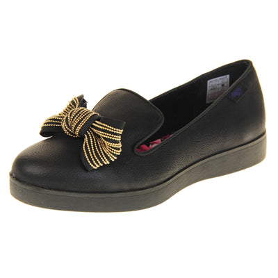 Rocket Dog slip on shoes. Loafer style shoes with a black faux leather upper. With a black and gold bow detail on the top of the foot. Bright floral patterned insole. Chunky black sole with slip resistant grip to the bottom. Left foot at an angle.