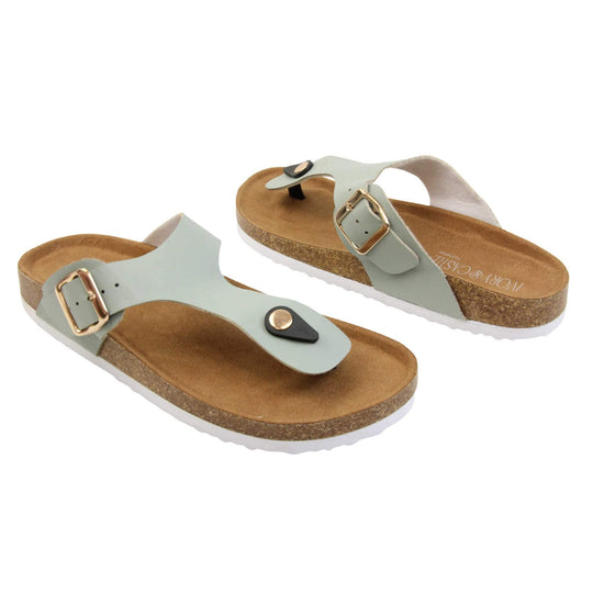 Sage flip flops. Sage green faux leather strap with toe post to the front and gold buckle to the outside. Soft tan faux suede footbed with cork effect outsole and white sole.  Both feet at an angle facing top to tail.