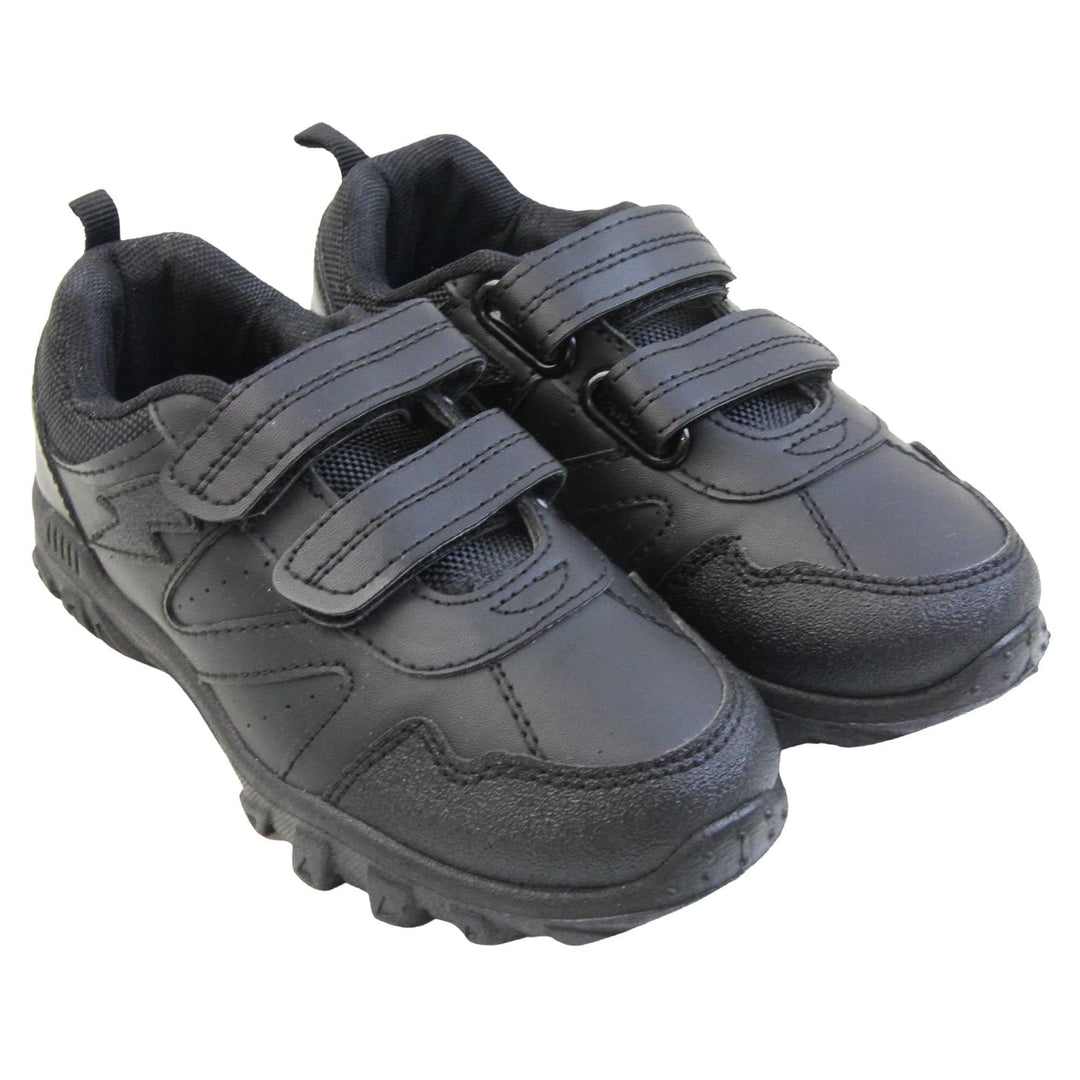 School trainers boy. Black faux leather trainers with zig zag detailing along the sides and a lightning bolt near the ankle. Two black touch fasten straps across the foot with a black textile lining. Chunky black soles. Both feet together at an angle.