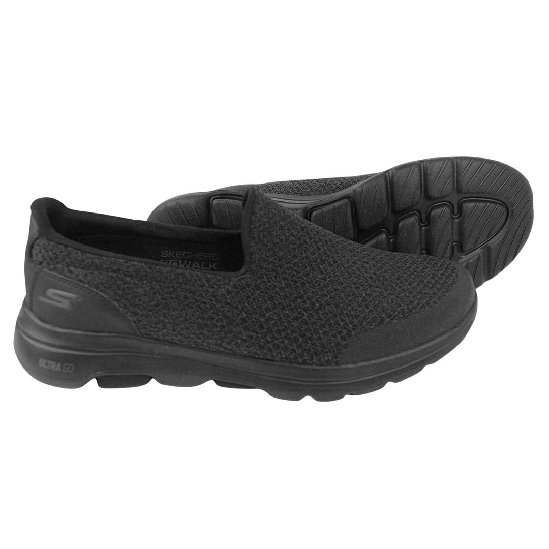 Skechers go walk five. Mens loafer style shoes with a trainer sole. Black woven mesh upper. Skechers S logo to the back. Black sole with grip to the bottom. Black textile lining. Both feet from a side profile with the left foot on its side to show the sole.