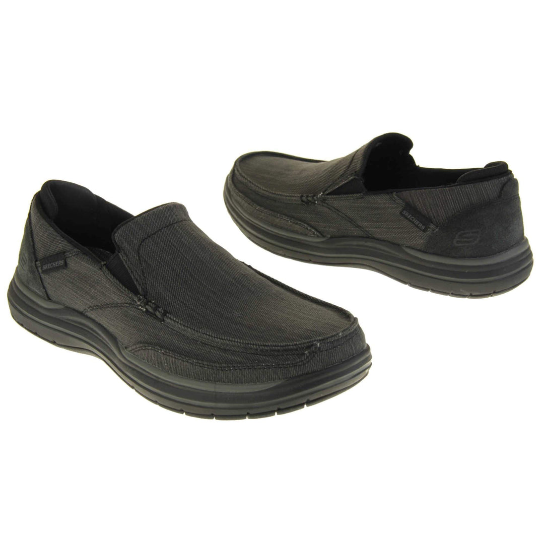Skechers Slip On. Black loafer trainers with black denim upper with stitching detail. Black tag to the outside ankle with Skechers written on. The heel is a faux suede with S logo on it. Chunky black sole with grip to the bottom. Both feet from an angle facing top to tail.