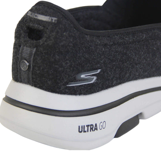 Skechers trainers. Loafer style shoes with a trainer sole. Black wool upper with elasticated panels by the tongue to give more flexibility and a better fit. Skechers S logo to the back. Chunky white sole with a black line running around it. Close up of the shoe to show the back of it and Skechers detail to the back.