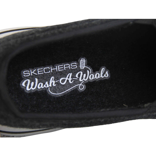 Skechers trainers. Loafer style shoes with a trainer sole. Black wool upper with elasticated panels by the tongue to give more flexibility and a better fit. Skechers S logo to the back. Chunky white sole with a black line running around it. Close up of the shoe to show the inside lining and Skechers wash a wool logo inside.