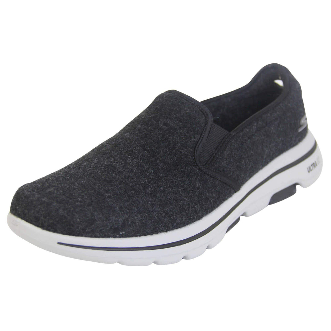 Skechers trainers. Loafer style shoes with a trainer sole. Black wool upper with elasticated panels by the tongue to give more flexibility and a better fit. Skechers S logo to the back. Chunky white sole with a black line running around it. Left foot at an angle.