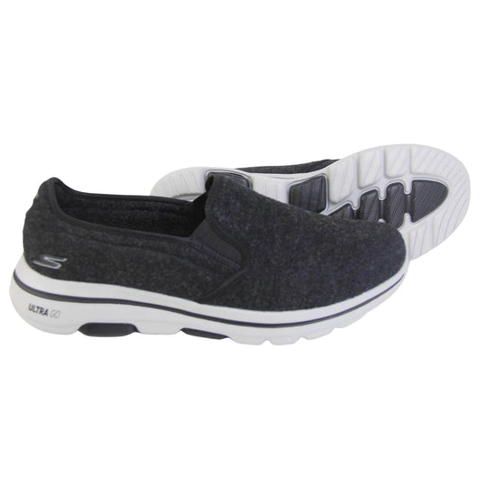 Skechers trainers. Loafer style shoes with a trainer sole. Black wool upper with elasticated panels by the tongue to give more flexibility and a better fit. Skechers S logo to the back. Chunky white sole with a black line running around it. Both feet from a side profile with the left foot on its side to show the sole.