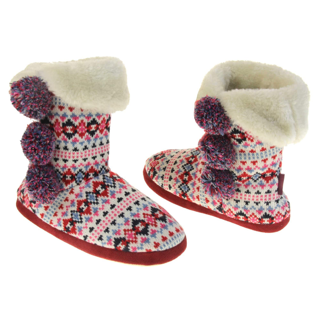 Slipper boots with hard sole. Multi coloured patterned knit upper in a Scandinavian or Aztec style with pom poms to the side, light beige plush faux fur trim and lining. Both feet at an angle, facing top to tail.