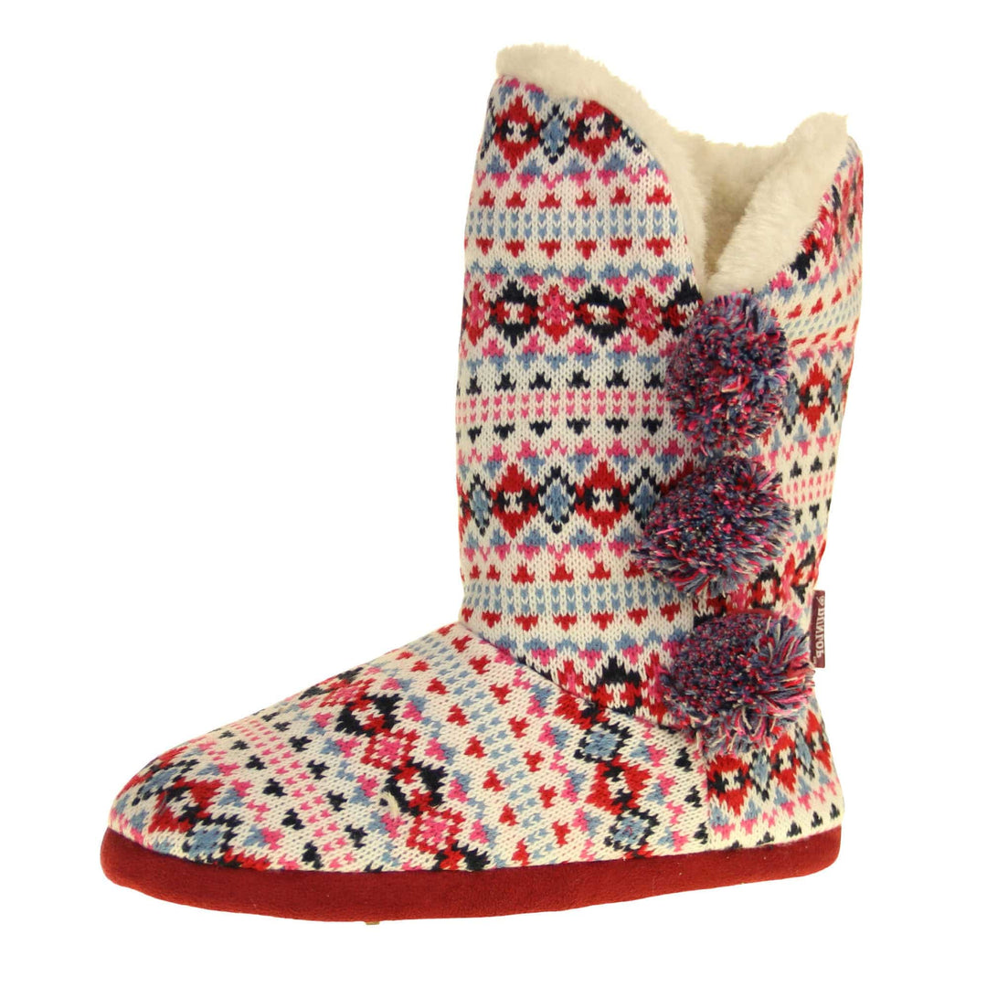 Slipper boots with hard sole. Multi coloured patterned knit upper in a Scandinavian or Aztec style with pom poms to the side, light beige plush faux fur trim and lining. Left foot taken at angle.