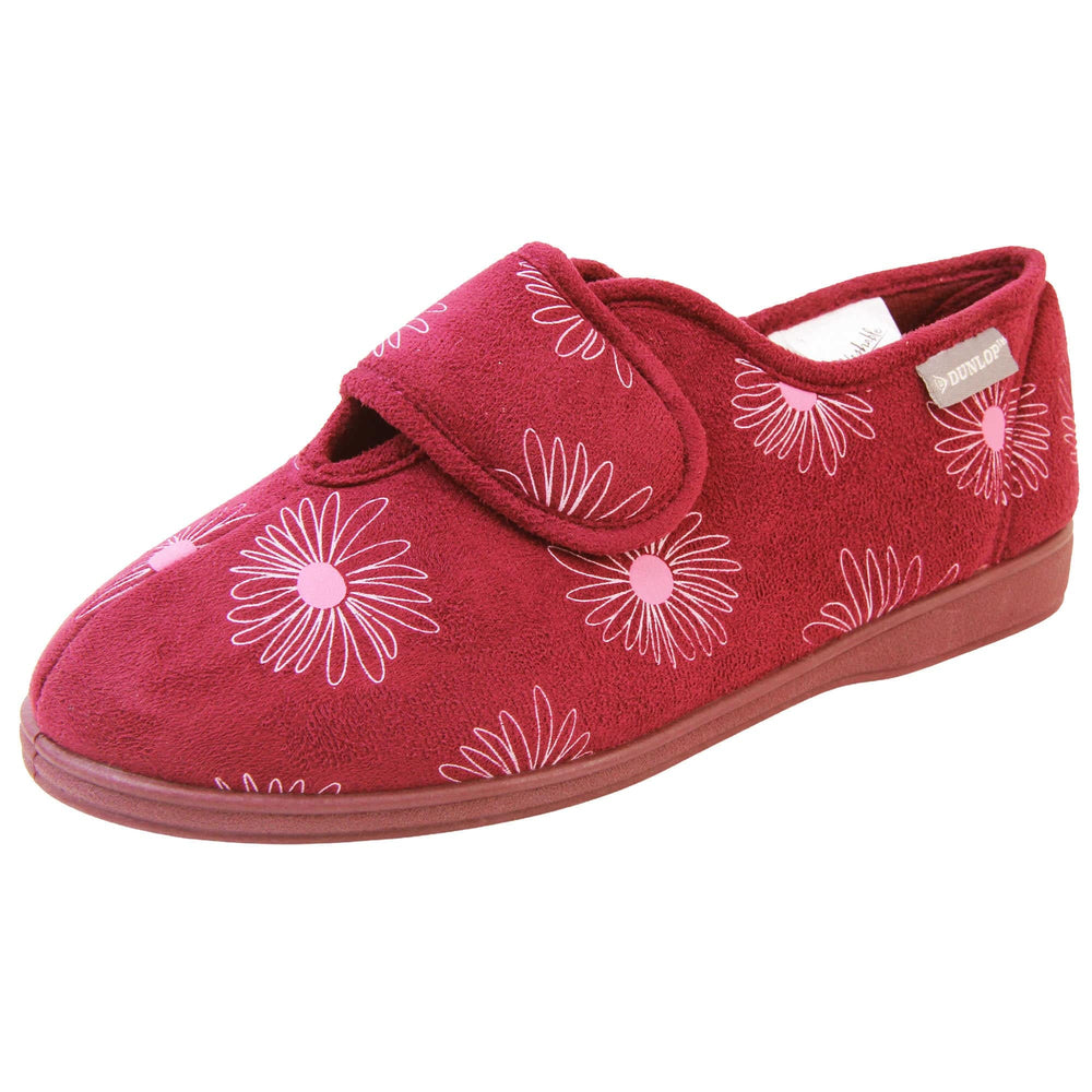 Slippers elderly women. Womens full back slipper. With a plum coloured upper with white daisy design and pink for the middle of the flowers. Touch fasten strap over the top of the foot to adjust the fit. Plum textile lining and firm plum sole. Left foot at an angle.
