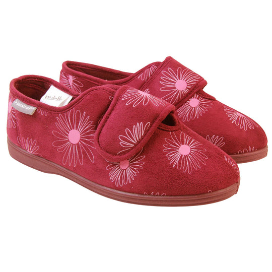 Slippers elderly women. Womens full back slipper. With a plum coloured upper with white daisy design and pink for the middle of the flowers. Touch fasten strap over the top of the foot to adjust the fit. Plum textile lining and firm plum sole. Both feet together at angle.