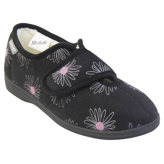 Slippers for elderly with swollen feet. Womens full-back slipper. Black upper with a white daisy design and pink for the middle of the flowers. Touch fasten strap over the top of the foot to adjust the fit. Cream fleece lining and firm black sole. Right foot at an angle.