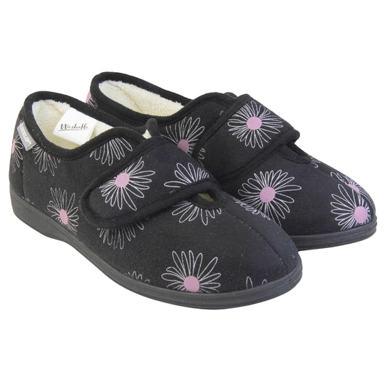 Slippers for elderly with swollen feet. Womens full-back slipper. Black upper with a white daisy design and pink for the middle of the flowers. Touch fasten strap over the top of the foot to adjust the fit. Cream fleece lining and firm black sole. Both feet together at an angle.