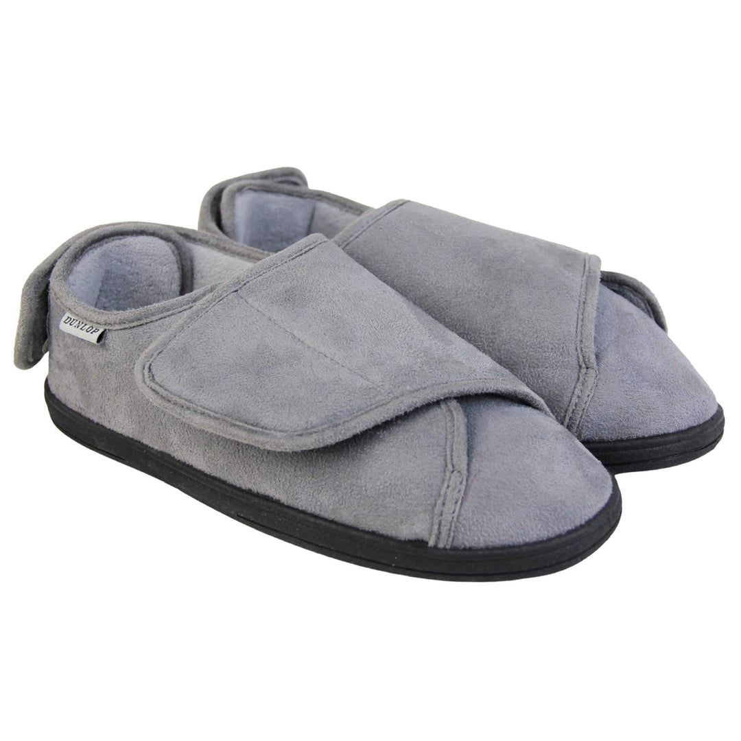 Mens adjustable slippers. Full back slippers with grey upper. Adjustable touch fasten strap to the top of the foot and around the back of the heel. Small white label on the outside rim, with Dunlop branding sewn in black. Grey faux fur lining. Firm black sole. Both feet together at an angle.