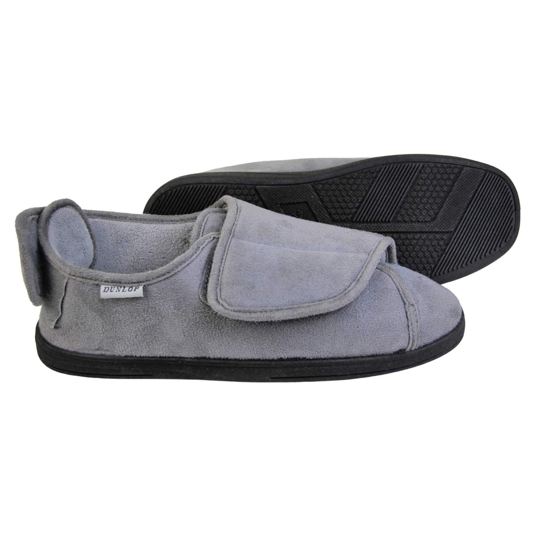 Mens adjustable slippers. Full back slippers with grey upper. Adjustable touch fasten strap to the top of the foot and around the back of the heel. Small white label on the outside rim, with Dunlop branding sewn in black. Grey faux fur lining. Firm black sole. Both feet from side profile with left foot on its side to show the sole.