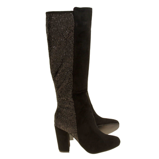 Sparkly knee high boots. Black faux suede upper with the back half of the boot covered in black glitter. Zip fastening down the inside leg of the boot. With a black block high heel and black sole.  Both feet from a side profile with the left foot on its side to show the sole.