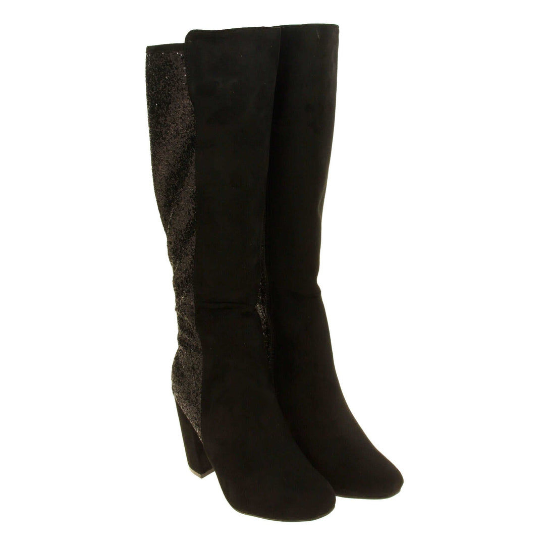 Sparkly knee high boots. Black faux suede upper with the back half of the boot covered in black glitter. Zip fastening down the inside leg of the boot. With a black block high heel and black sole. Both feet together from an angle.