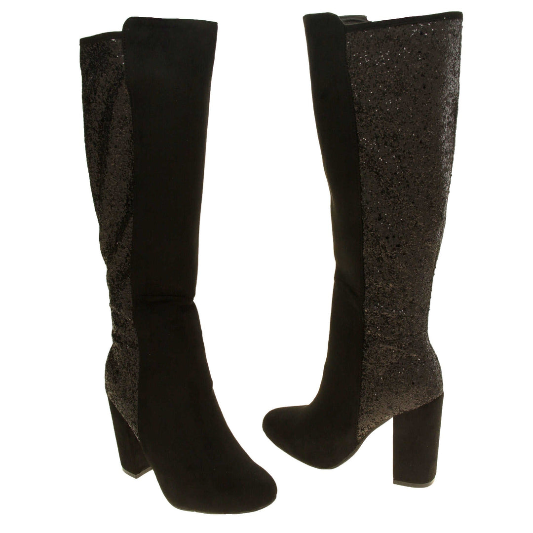 Sparkly knee high boots. Black faux suede upper with the back half of the boot covered in black glitter. Zip fastening down the inside leg of the boot. With a black block high heel and black sole. Both feet from a slight angle facing top to tail.