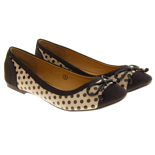 Spotty Shoes. Womens ballerina style shoes with a glossy cream upper with black polka dots covering it. Black faux suede toes and heels and a black bow to the top. Nude faux-leather  lining. Black sole with very slight heel. Both feet together at a slight angle.