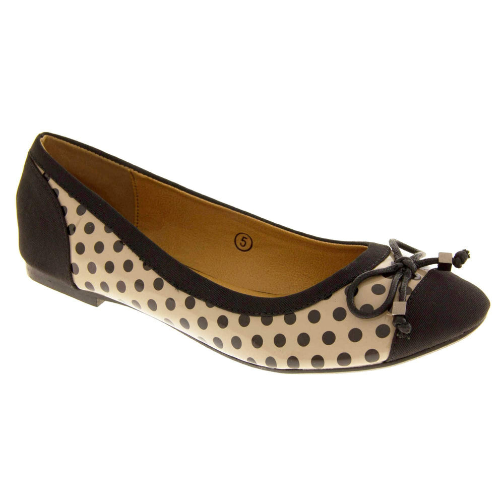 Spotty Shoes. Womens ballerina style shoes with a glossy cream upper with black polka dots covering it. Black faux suede toes and heels and a black bow to the top. Nude faux-leather  lining. Black sole with very slight heel. Right foot at an angle.