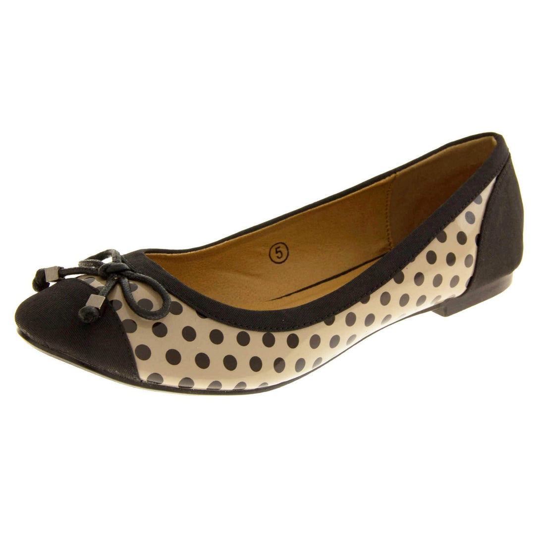 Spotty Shoes. Womens ballerina style shoes with a glossy cream upper with black polka dots covering it. Black faux suede toes and heels and a black bow to the top. Nude faux-leather  lining. Black sole with very slight heel. Left foot at an angle.