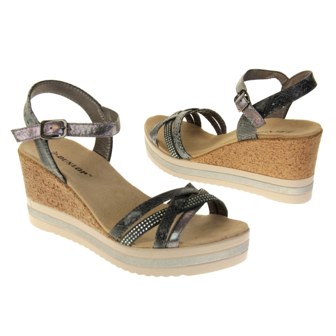 Strappy wedge sandals. Pewter coloured, faux leather strappy upper. The toe straps. are a mix between plain, faux snake skin and studded. Ankle strap is faux snakeskin. Nude faux suede cushioned insoles with black Dunlop branding. Cork wedge heel and platform sole made up of nude and white contrasting strips. Both feet at an angle facing top to tail.