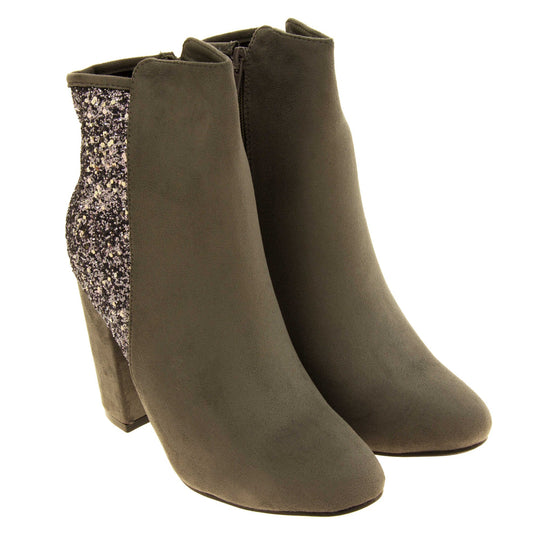 Suede ankle boots women. Grey faux suede upper with the back half of the boot covered in silver glitter. Zip fastening down the inside leg of the boot. With a grey block high heel and black sole. Both feet together from an angle.